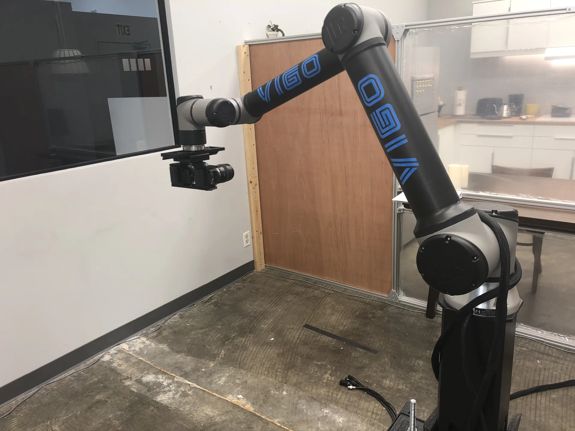 The full length of the robotic arm extended across the room toward the camera rig, with a wooden door behind.