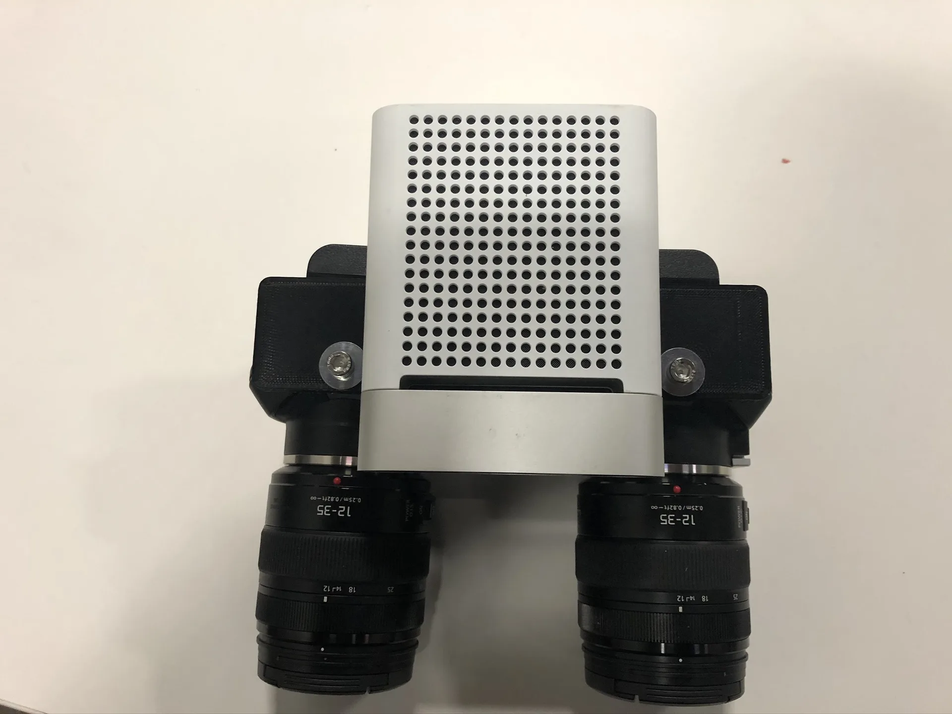 Top-down view of the stereo cage on a white surface, with a grey perforated RGB and depth sensor between the two cameras and the lenses pointing down.