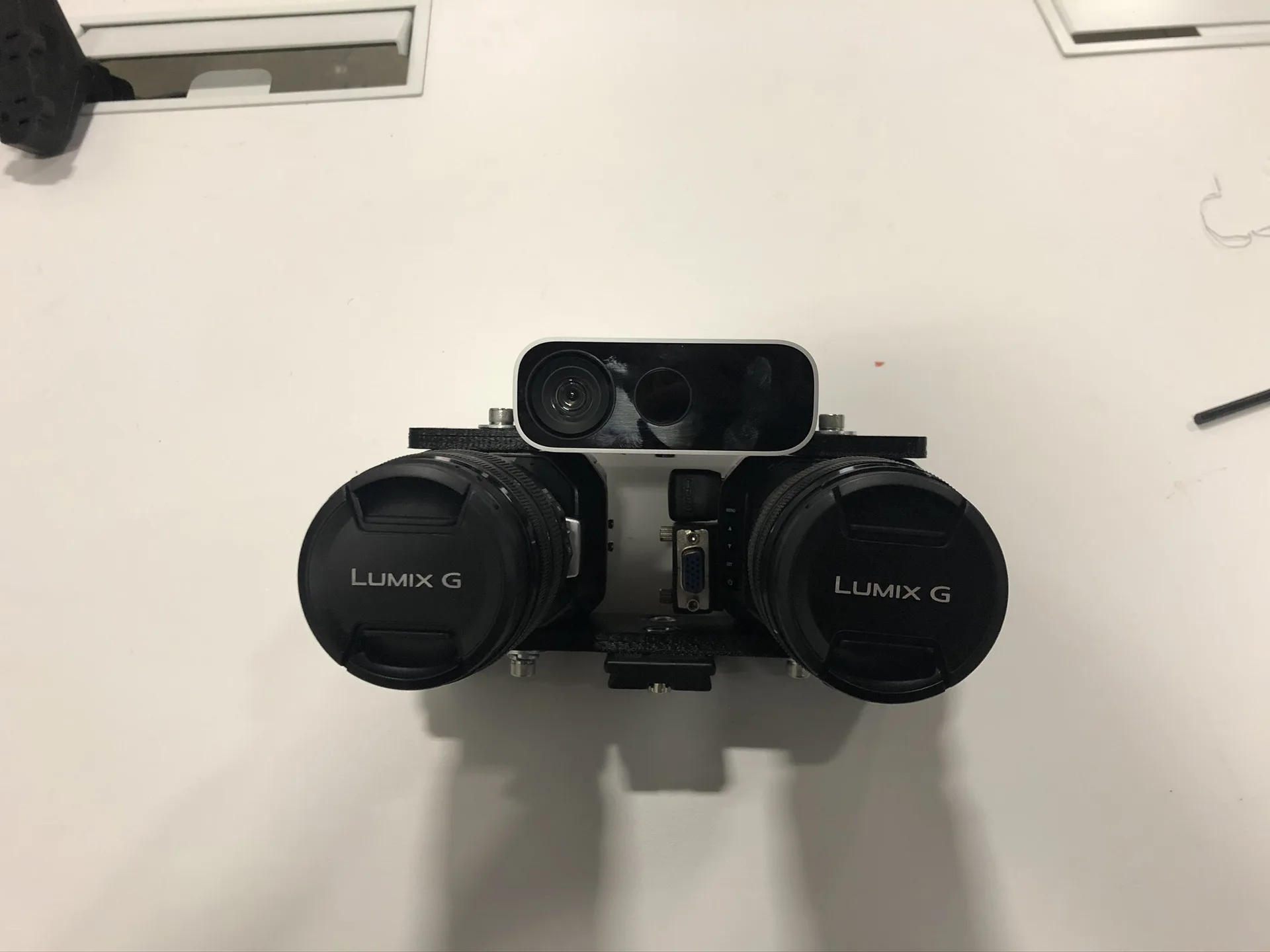 Front view of the stereo rig against a white wall: two camera lenses side by side in a black printed cage, with a grey RGB and depth sensor mounted above them.
